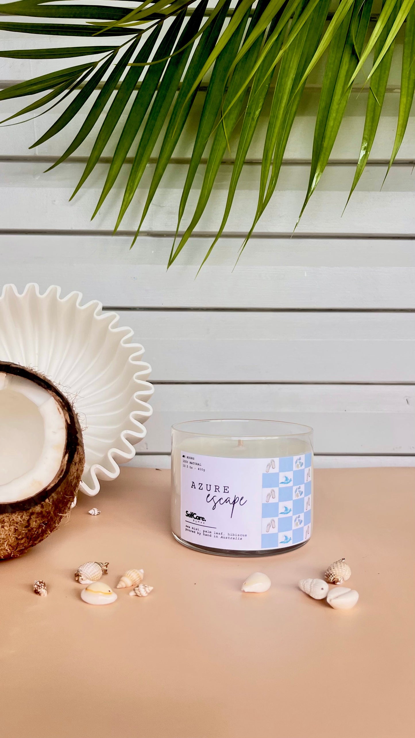 Candle labeled 'Azure Escape' with a coconut and palm leaves on a wooden surface