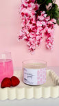 Candle labeled 'Island Sweet' with pink flowers and a glass of pink liquid on a light pink background