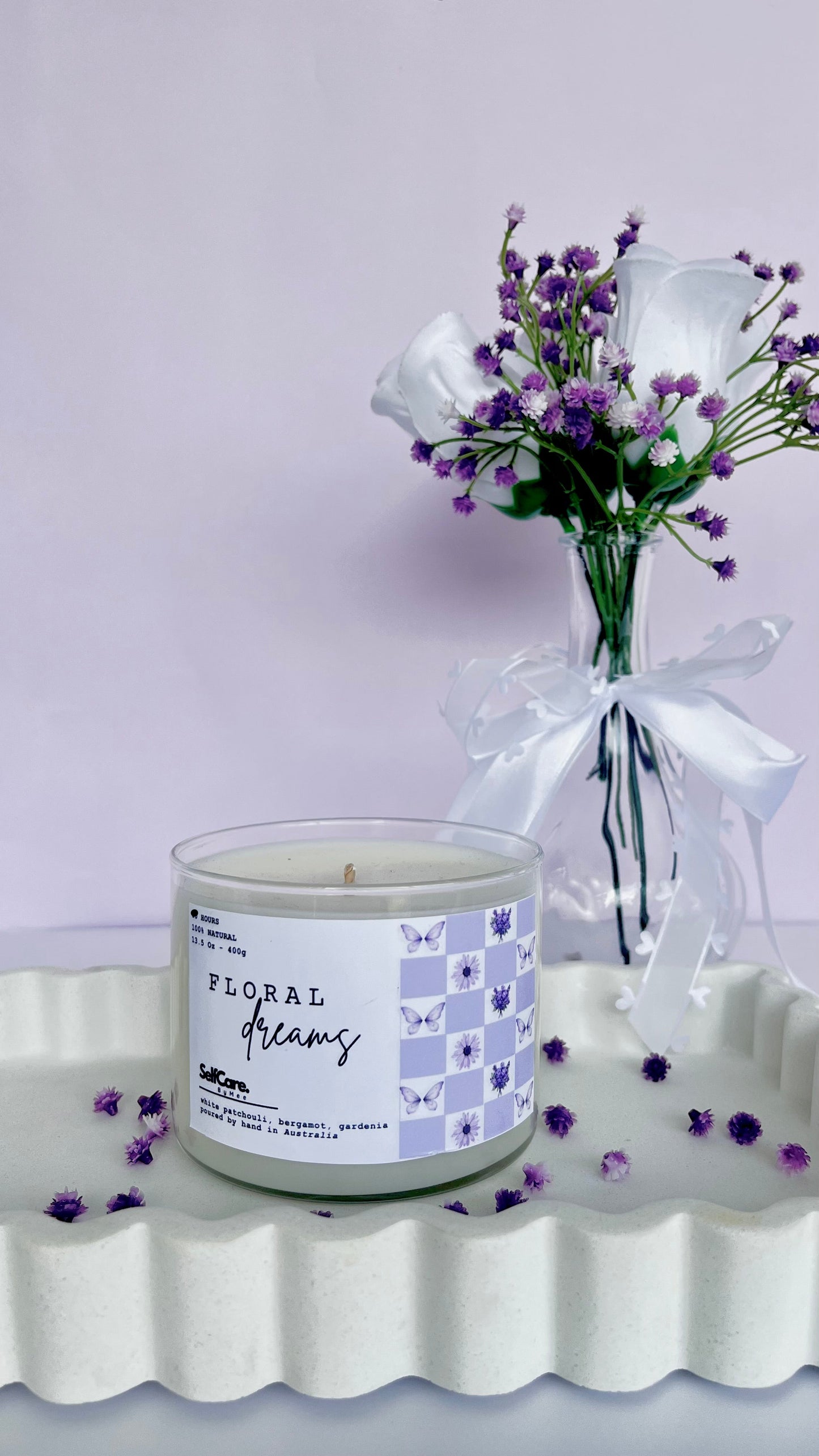 Candle labeled 'Floral Dreams' with a small bouquet of flowers on a white surface.