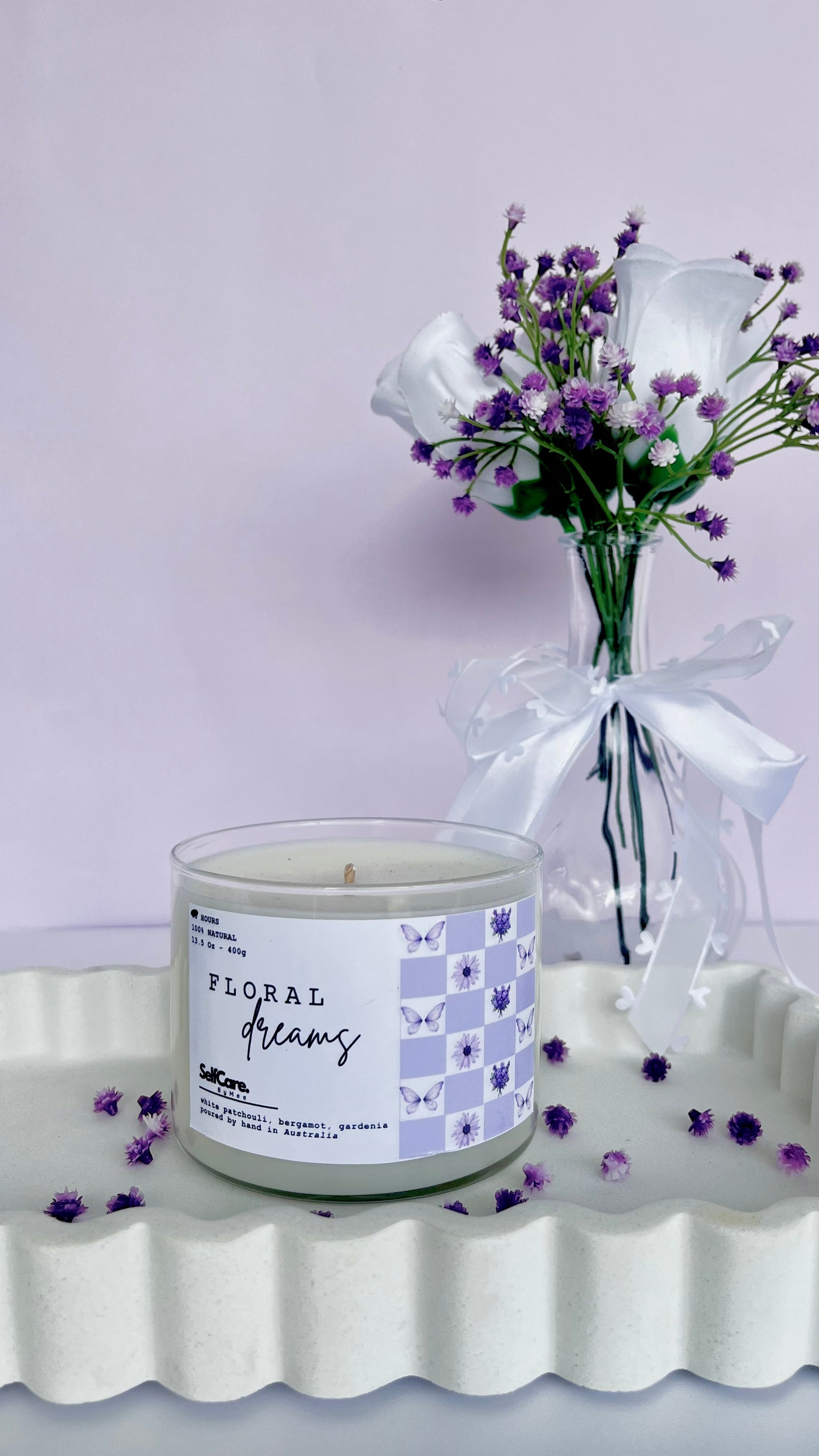 Candle labeled 'Floral Dreams' with a small bouquet of flowers on a white surface.