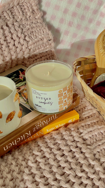 Candle with a label on a textured surface with books and a knitted item.