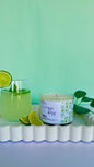 Candle labeled 'Citrus Bliss' next to a glass of lemonade with lime slices on a green background