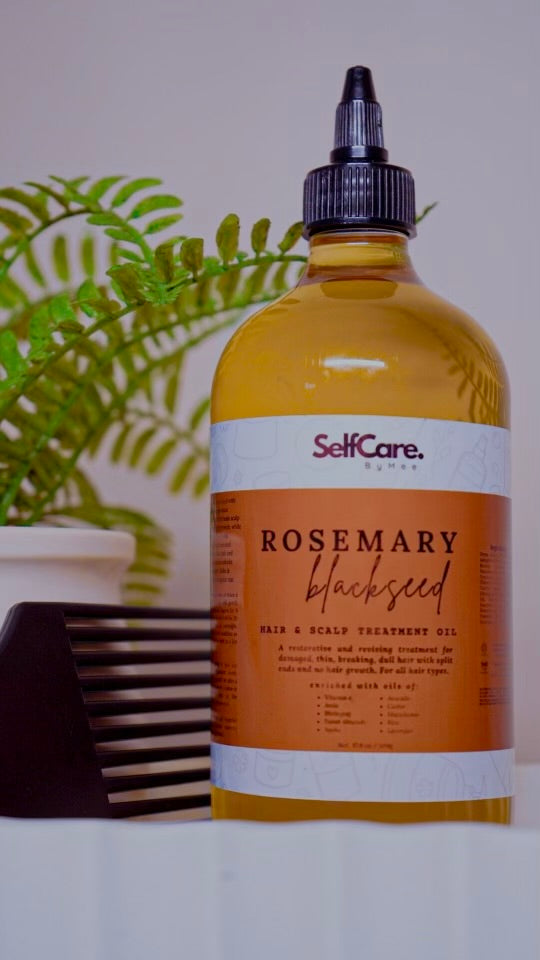Bottle of SelfCare Rosemary Blackseed hair and scalp treatment oil with a comb and plant in the background.