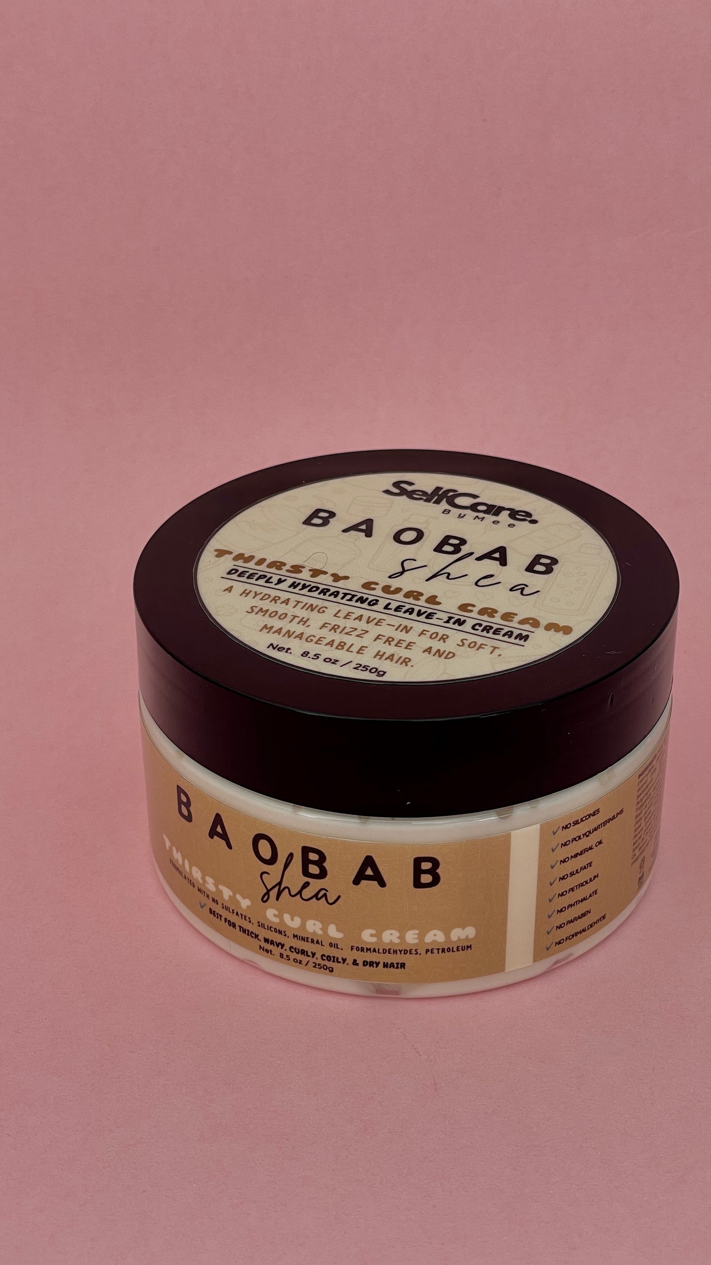 A jar of SelfCare by Mee Baobab Shea Moisture Curl Cream with a dark brown lid and beige label, set against a solid pink background.