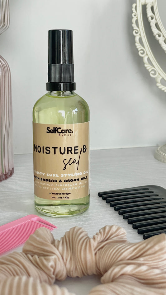SelfCare by Mee Moisture & Seal thirstly curl styling oil in a pump bottle with a beige label and black pump top, styled on a white surface with a pink comb, black wide tooth hair comb, and beige scrunchie in the foreground