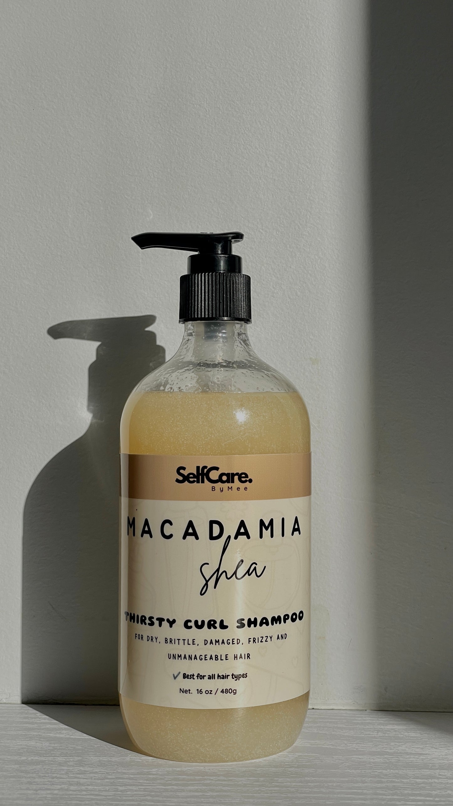 A bottle of SelfCare by Mee Macadamia Shea Thirsty Curl Shampoo with a black pump dispenser, set against a neutral gray background with a soft shadow.