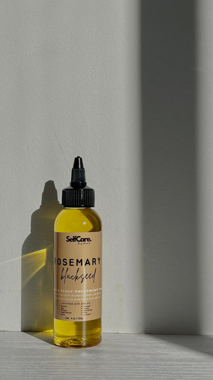 A bottle of SelfCare by Mee Rosemary Blackseed hair oil with a black dropper cap, filled with yellow oil, set on a light gray surface with dramatic diagonal shadows.