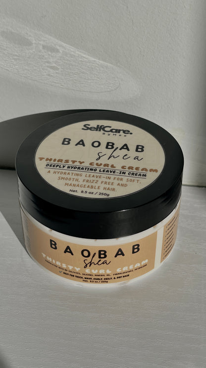 A jar of SelfCare by Mee Baobab Shea Thirsty curl Leave-In Cream with a black lid and beige label, photographed on a light textured surface with a soft shadow.